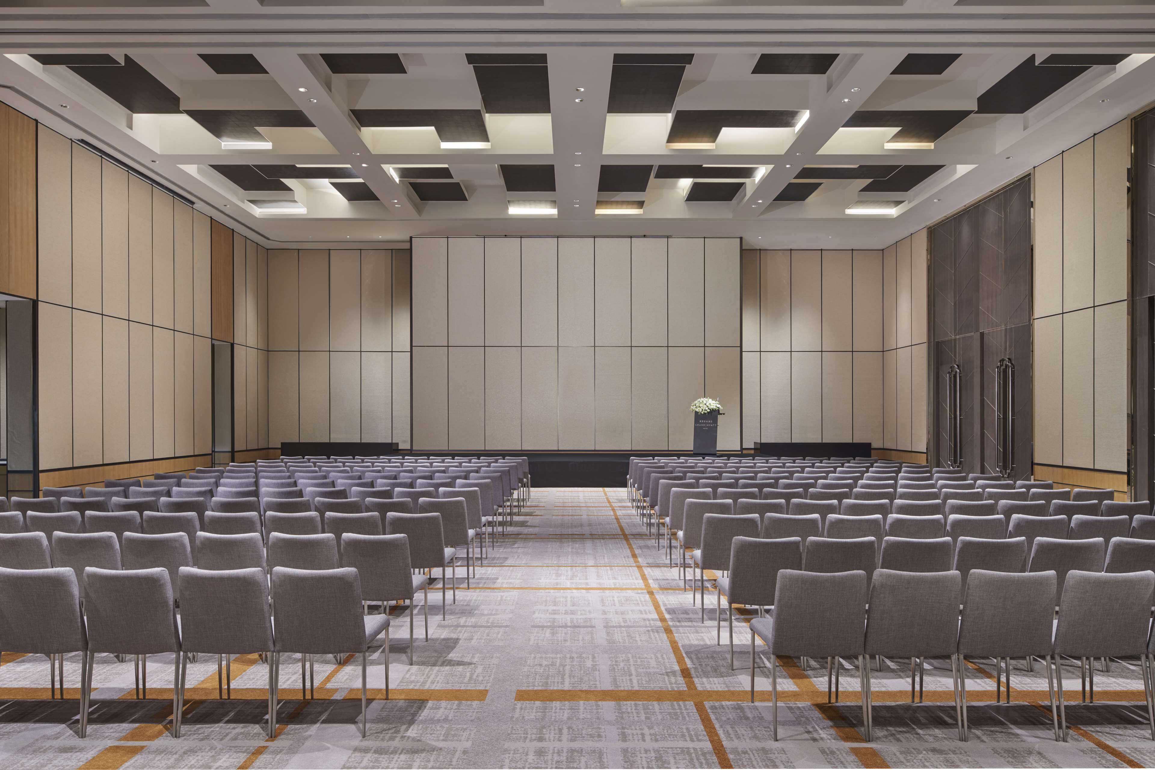 Un salón de conferencias con filas de sillas, un atril y suelo alfombrado.