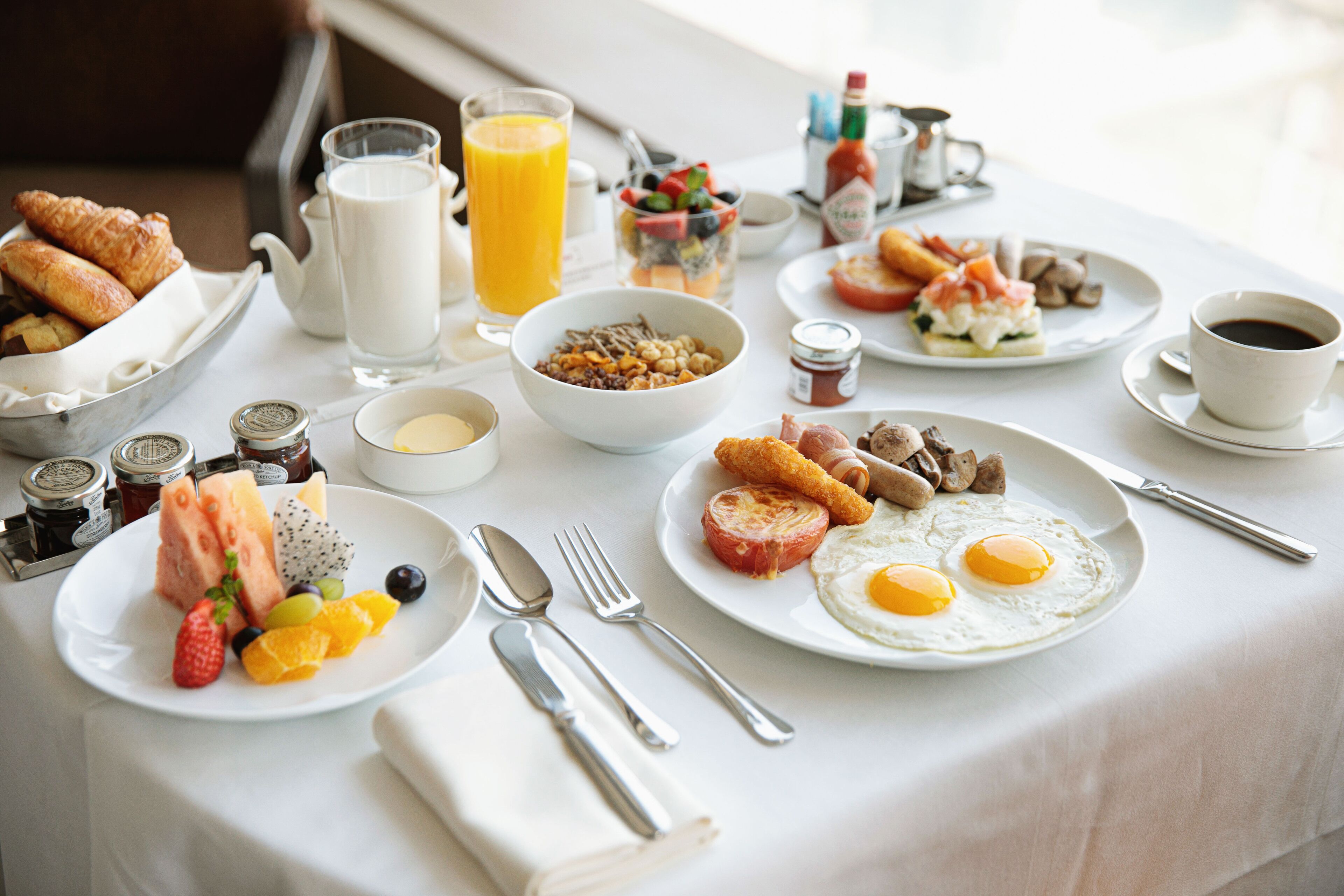 A breakfast table with croissants, fruits, eggs, and coffee.