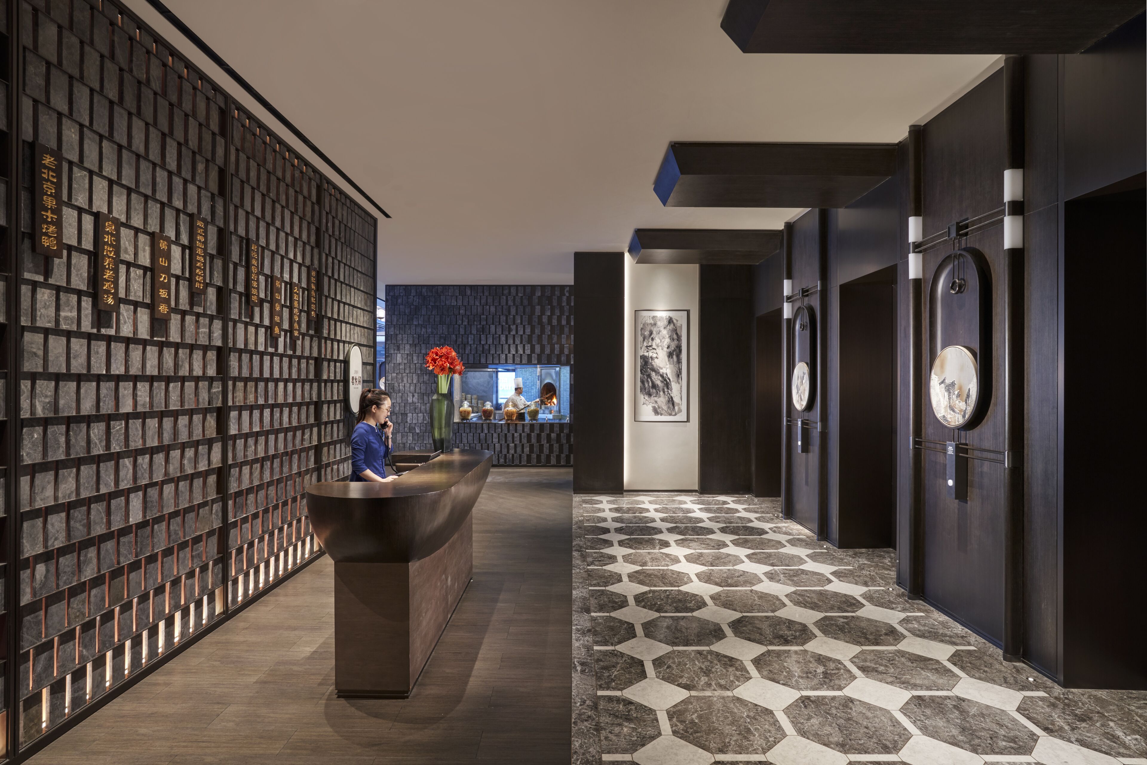 A reception area with a reception desk, a wall with vertical text, a patterned floor, and a wall-mounted clock.