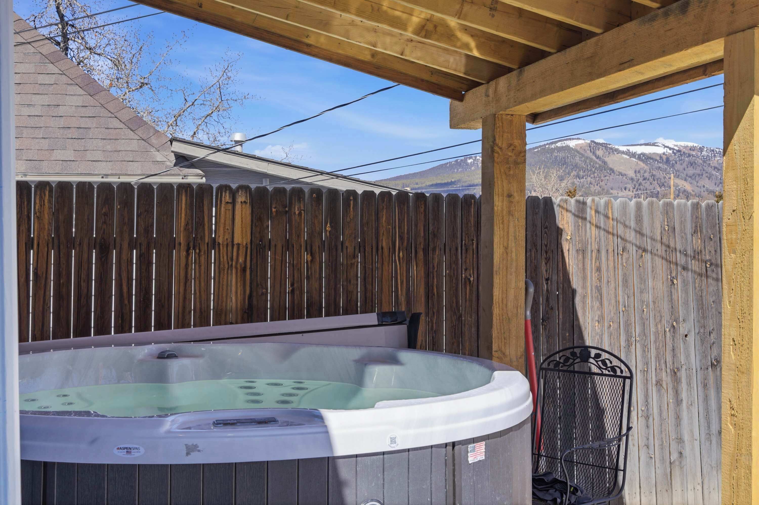 A hot tub under a wooden pergola with a wooden fence in the background.