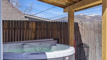 A hot tub under a wooden pergola with a wooden fence in the background.