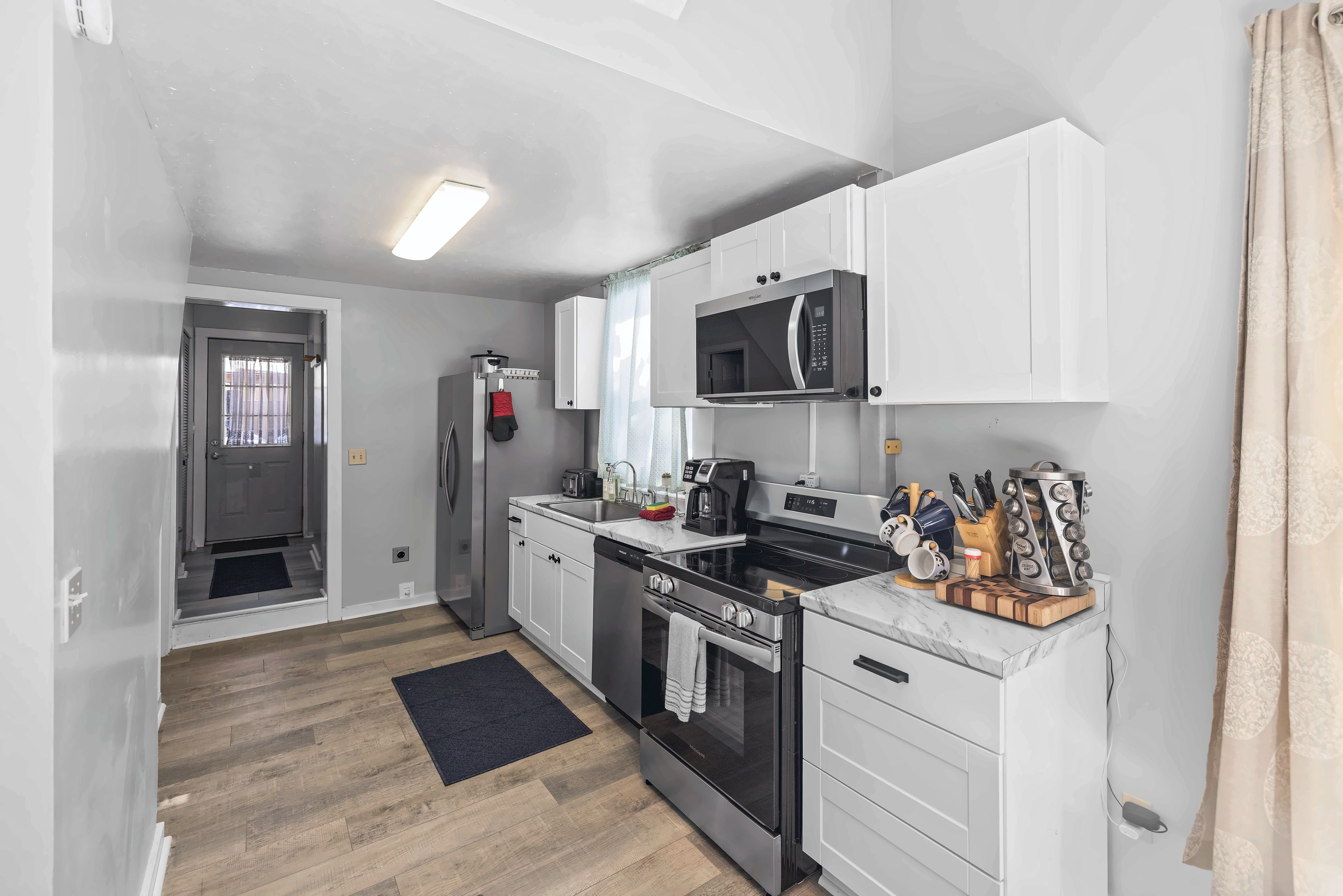 A compact kitchen with white cabinetry, a microwave, a stove, and a coffee maker.
