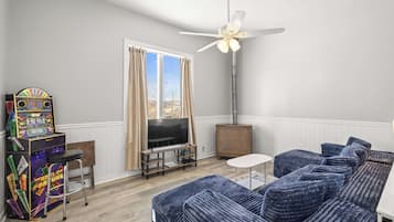 Un salon avec un canapé bleu, un téléviseur, un ventilateur de plafond et un juke-box.