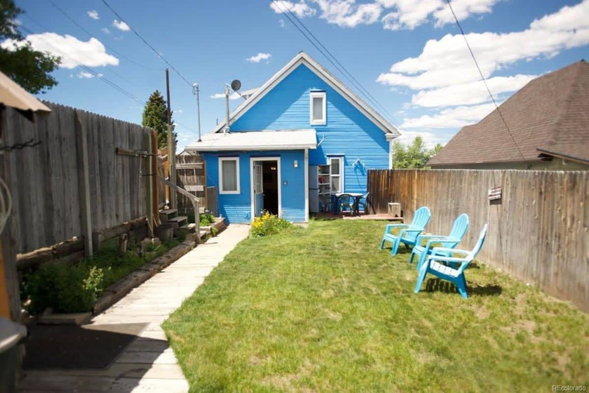 Een blauw huis met een houten omheining, een gazon en blauwe stoelen.