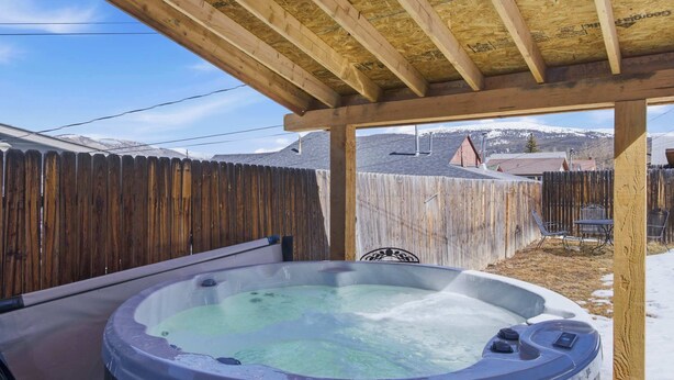 Ein Whirlpool unter einer Holzw pergola, mit Holzzaun und Bergen im Hintergrund.