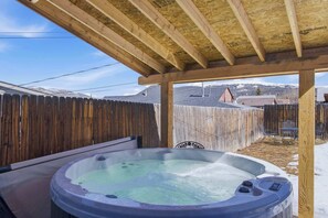 Ein Whirlpool unter einer Holzw pergola, mit Holzzaun und Bergen im Hintergrund.