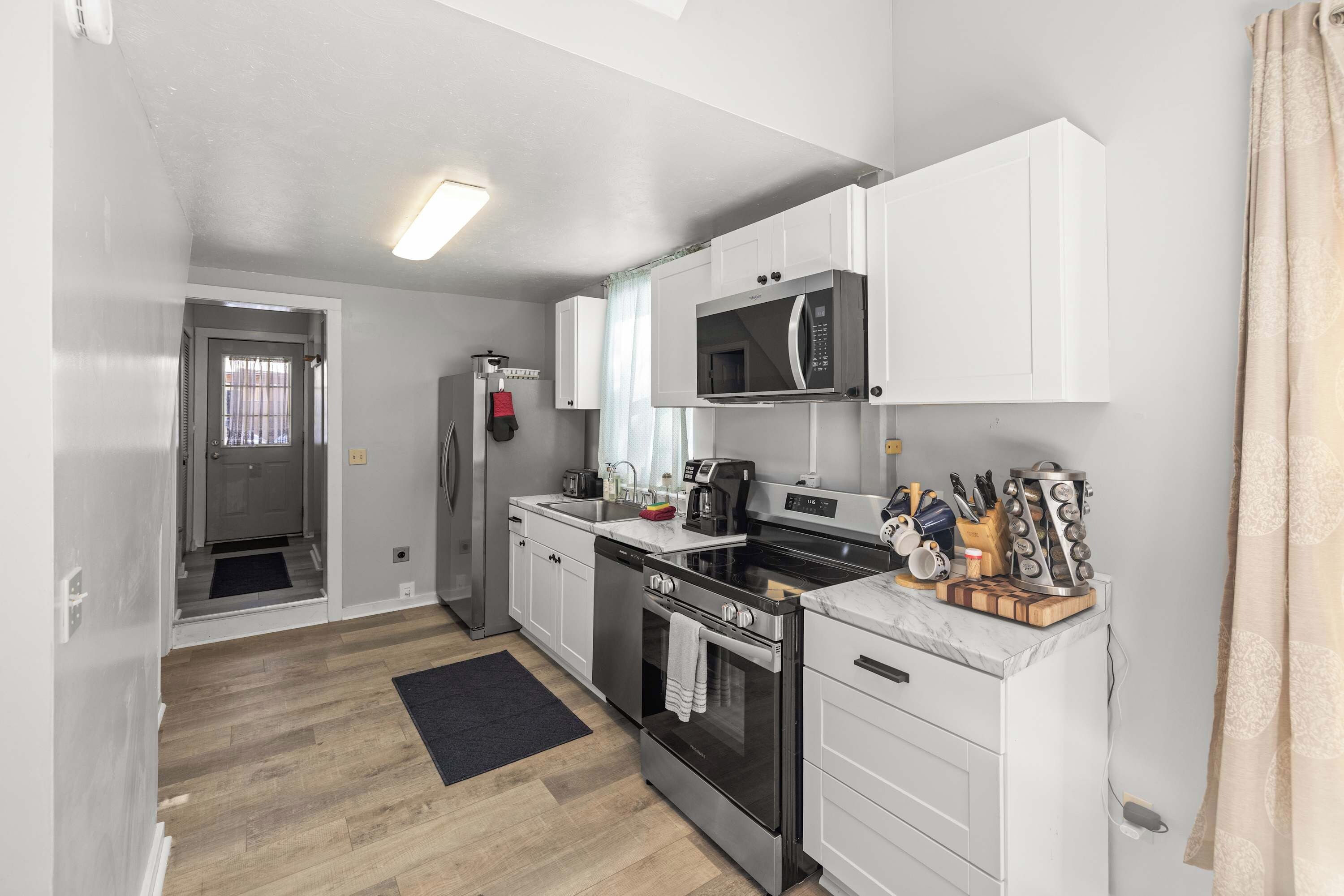 A compact kitchen with white cabinets, a microwave, a stove, and a sink.