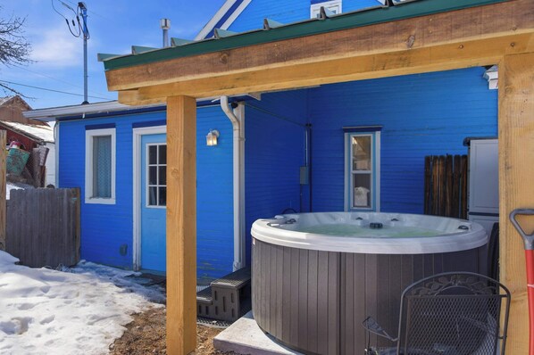 Ein blaues Haus mit Whirlpool, Holzterrasse und überdachter Terrasse.