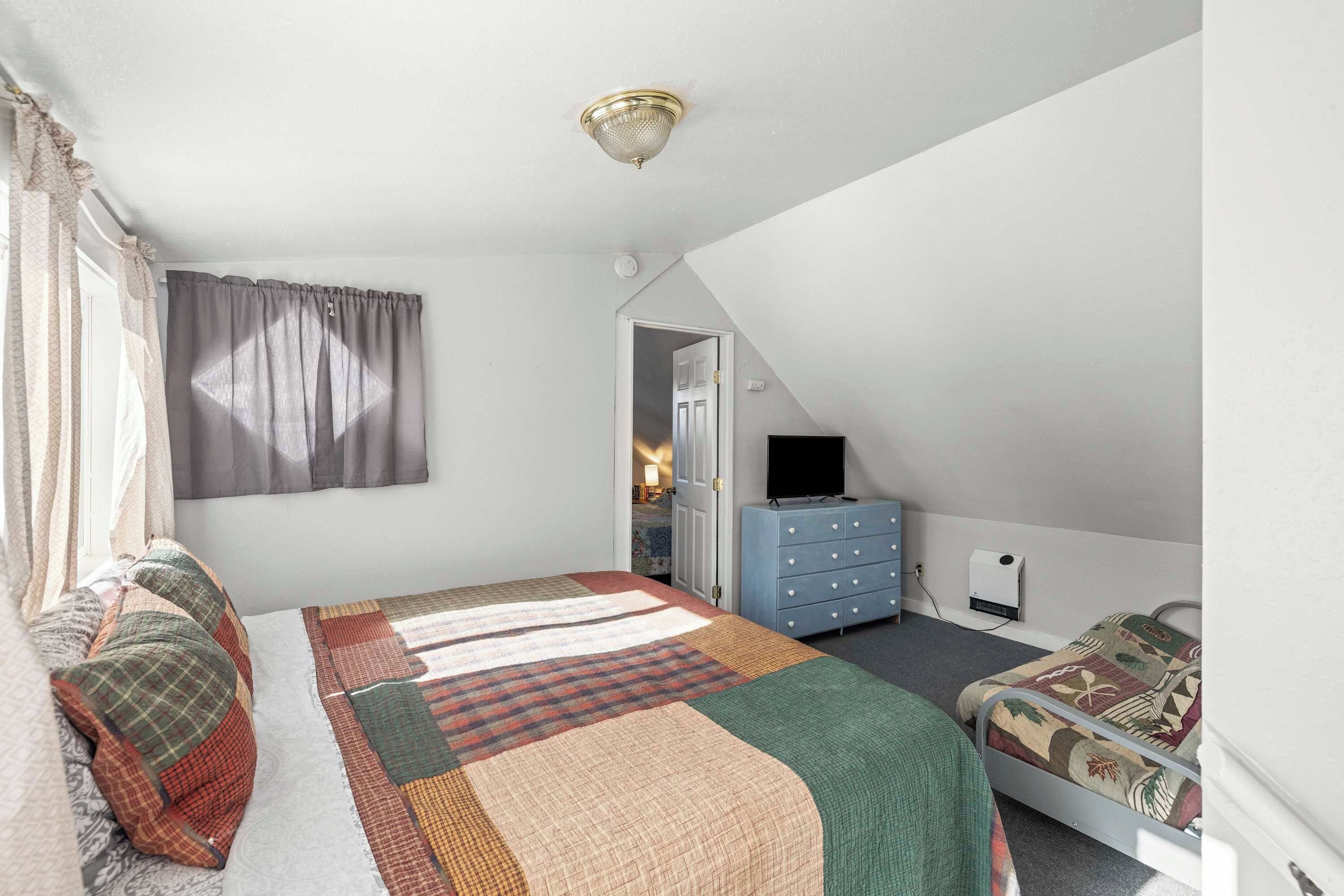 Een slaapkamer met een bed, een dressoir, een televisie en een deur naar een andere kamer.