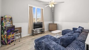 Ein Wohnzimmer mit einem blauen Sofa, einem Fernseher, einem Deckenventilator und einer Jukebox.