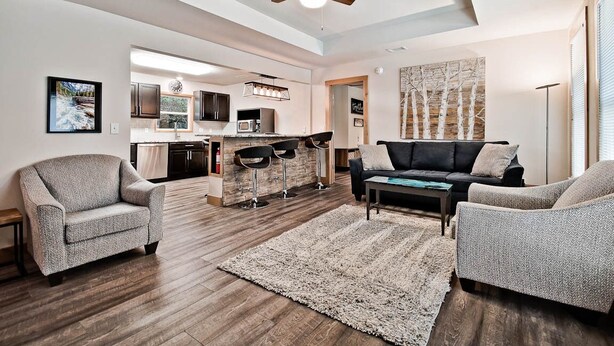 Een ruime woonkamer met een moderne keuken op de achtergrond, een plafondventilator en een groot kunstwerk aan de muur.