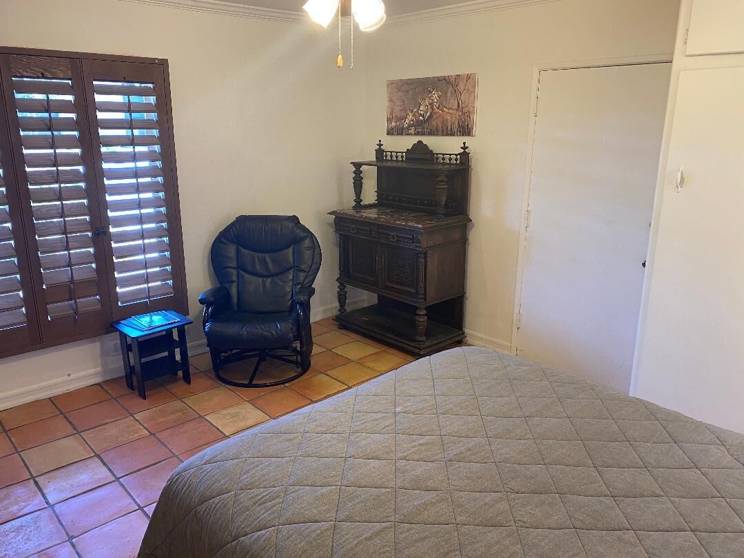 Une chambre à coucher avec un lit, une chaise, une petite table, un bureau et un tableau accroché au mur.