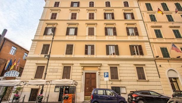 Un hôtel à plusieurs étages, doté d’une façade classique, d’une entrée bien visible et d’un panneau indiquant la présence d’un parking.