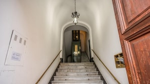Un escalier avec une rampe métallique, un luminaire suspendu et une porte en bois en haut.