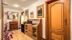 Un couloir avec un plancher en bois, une armoire en bois avec des tiroirs, un bureau avec un ordinateur et une porte.