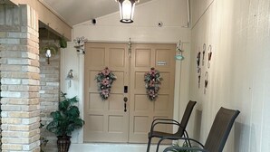 Une entrée propre et bien entretenue, avec un mur en briques, deux portes, un luminaire suspendu et un banc agrémenté d’un pot de fleurs.