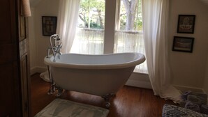 A bathroom with a freestanding bathtub, a window with sheer curtains, and a wooden floor. - Romantic Slipper Tub (Carmine)