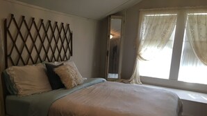 A bedroom with a bed, a headboard, a window with curtains, and a mirror. - Romantic Slipper Tub (Carmine)