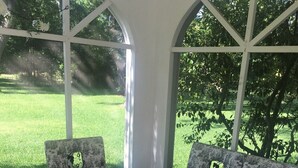 A covered patio with a patterned sofa and armchair, a small round table, and a view of a green lawn. - Romantic Slipper Tub (Carmine)