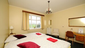 A hotel room with a large bed, a desk, a chair, a mirror, and a window with curtains. - Ársalir Guesthouse (Vik I Myrdal)