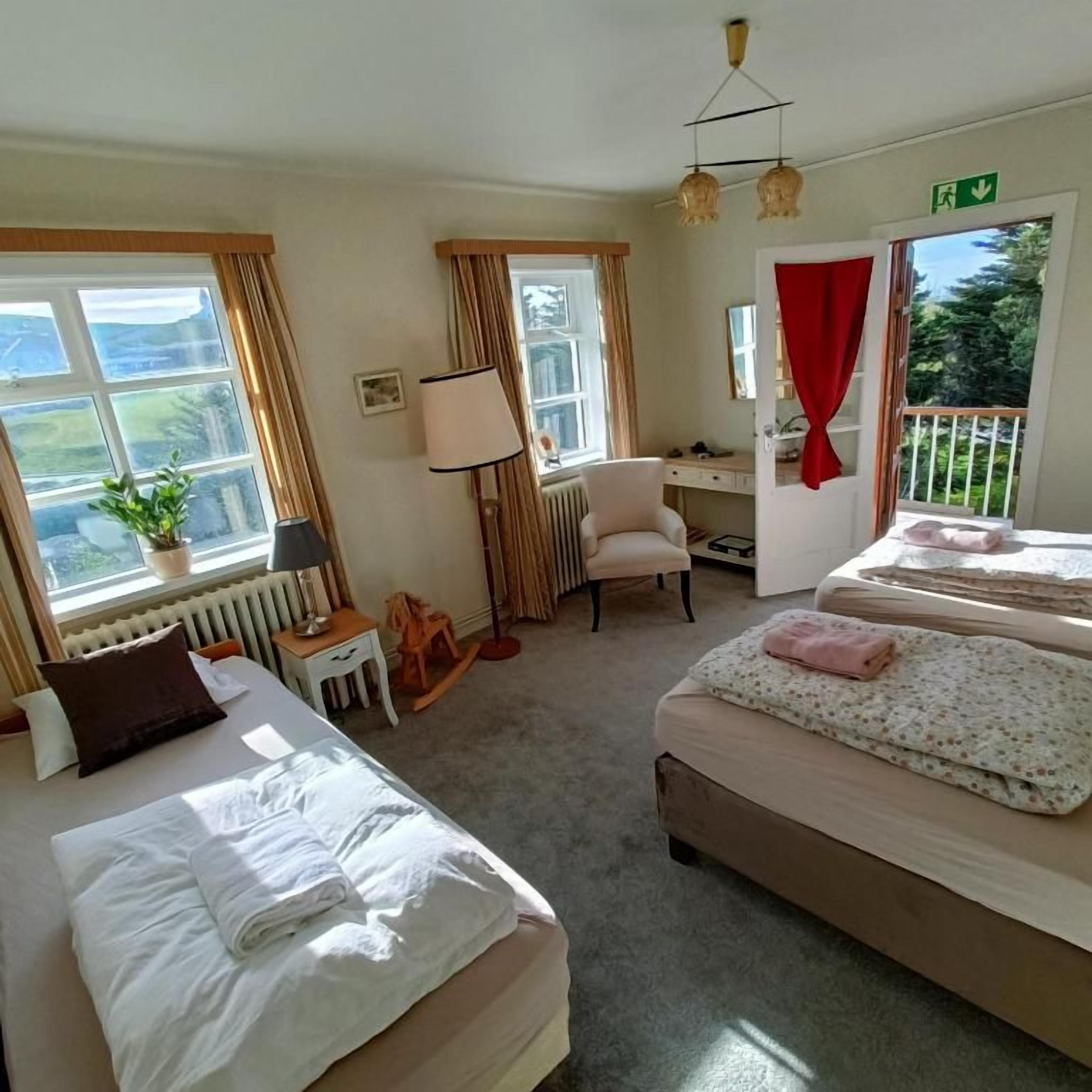 A hotel room with two beds, a desk, a chair, and a view of the outdoors.