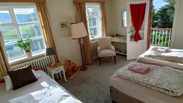 A hotel room with two beds, a desk, a chair, and a view of the outdoors.