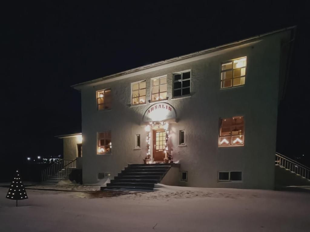 A building with a sign that reads 'HUSALI' at the entrance, a staircase leading up to the door, and a snow-covered ground.