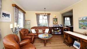 A living room with leather armchairs, a coffee table, a bookshelf, and a dining area with a wooden table and chairs. - Ársalir Guesthouse (Vik I Myrdal)