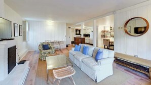 A modern living room with a sofa, coffee table, and chairs. There is a fireplace, a television, and a kitchen area in the background. - Fabulous Classic Victorian Home in Pacific Heights (San Francisco)