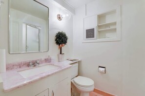 A bathroom with a white sink, a mirror, a toilet, and a small shelf with toiletries. - Fabulous Classic Victorian Home in Pacific Heights (San Francisco)