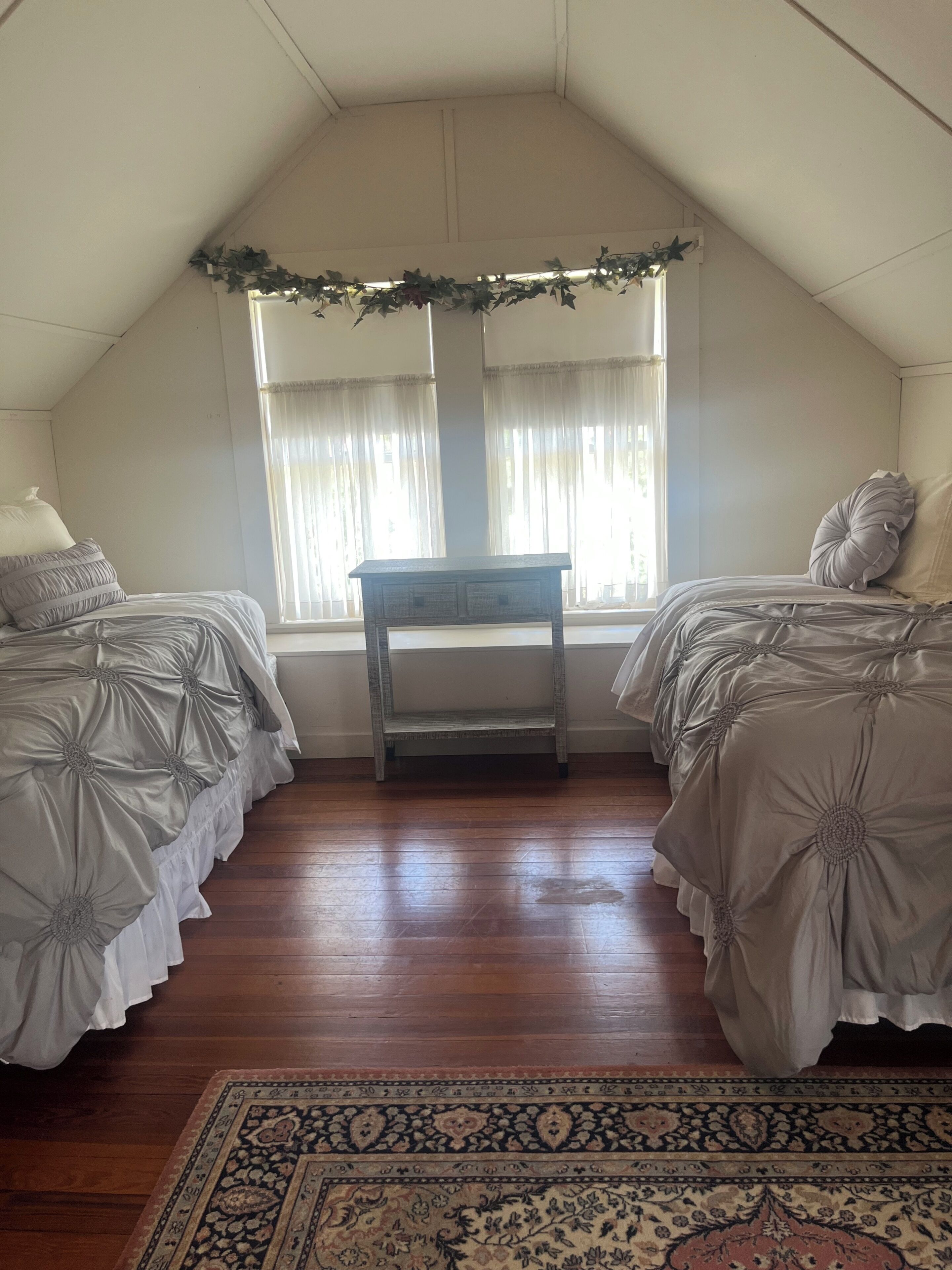 Een slaapkamer met twee bedden, een houten tafel en een groot raam met gordijnen.