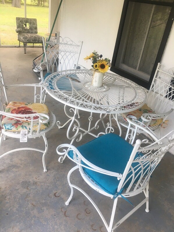 Un espace patio avec une table ronde en métal et des chaises en métal blanches, dont certaines sont agrémentées de coussins à motifs floraux.