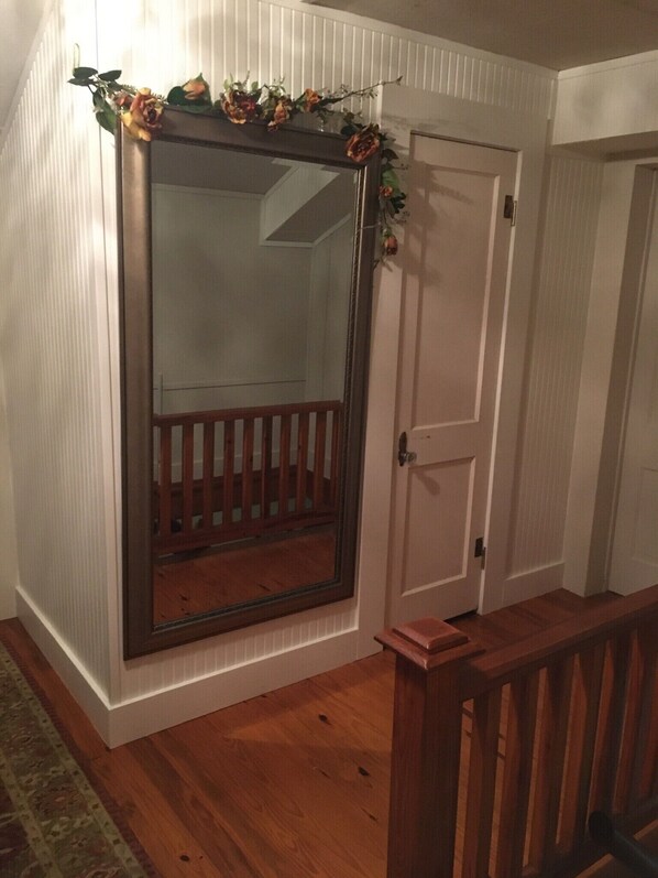 A room with a large mirror, wooden flooring, a white door, and a small wooden bench. - Sleeps 4, shared bath (Carmine)