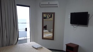 A hotel room with two beds, a television, an air conditioning unit, and a view of the sea through the window. - Hotel Nolasco (Macaé)