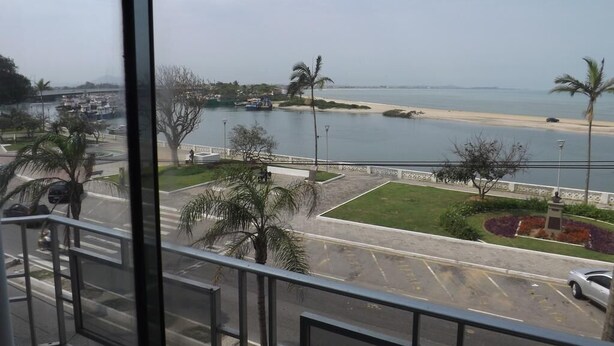 A view from a window overlooking a beach with a parking area and a road. - Hotel Nolasco (Macaé)