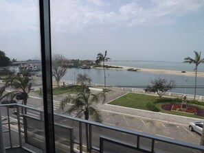 Vista desde una ventana sobre una playa, un estacionamiento y una carretera.