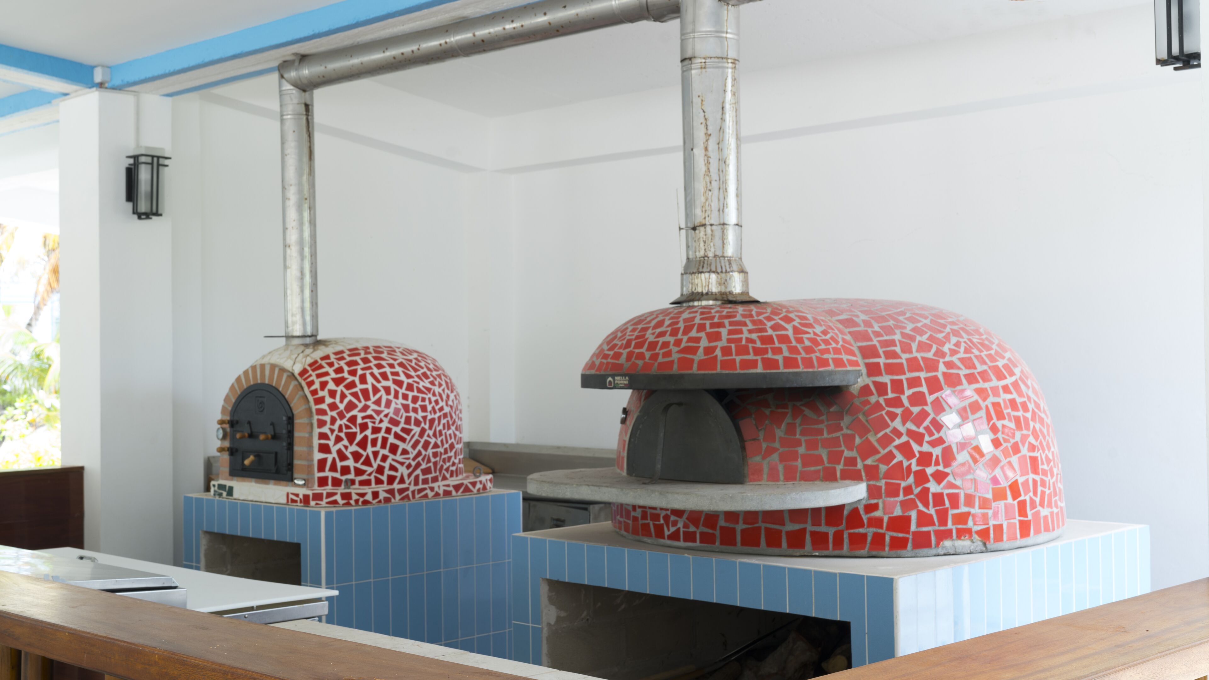 Una cocina con dos hornos de azulejos rojos, un salpicadero de azulejos azules y una encimera de madera.