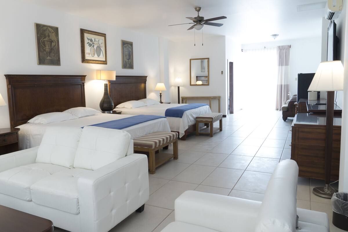 A hotel room with two beds, a sofa, a chair, a desk, and a TV.