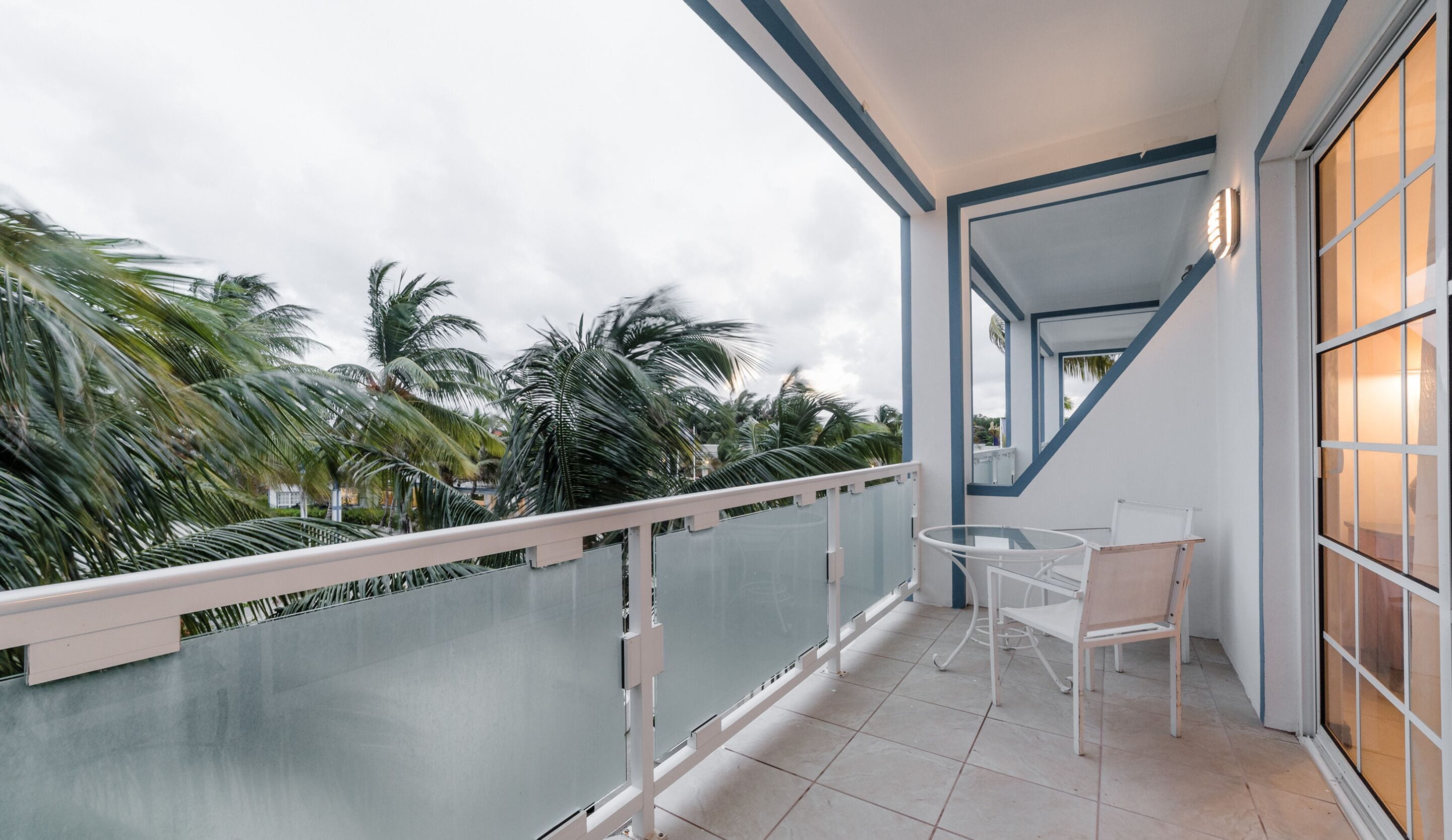 Un balcone con ringhiera in vetro, un tavolo e due sedie.