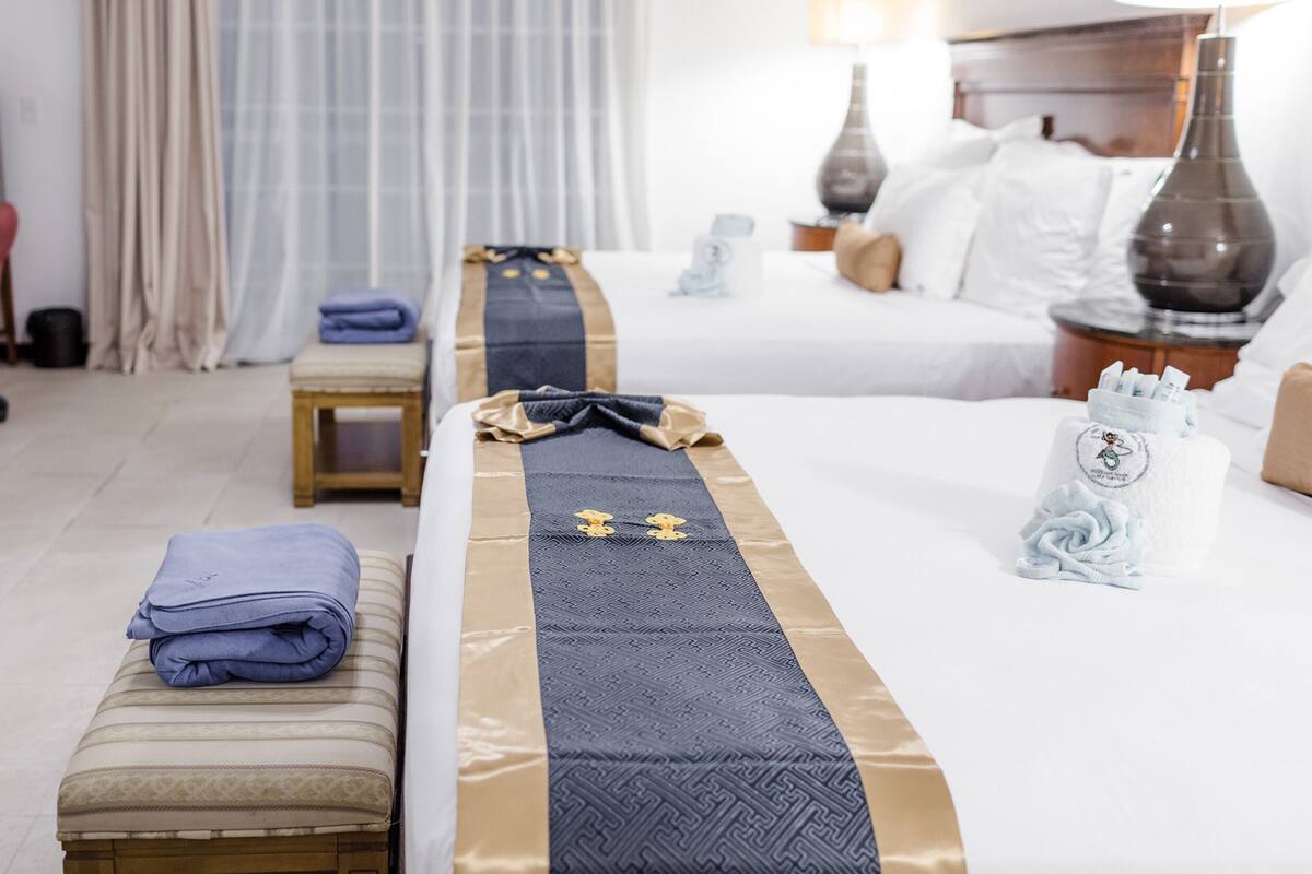 A hotel room with a neatly made bed, a small bedside table, a chair, a desk, and a TV.