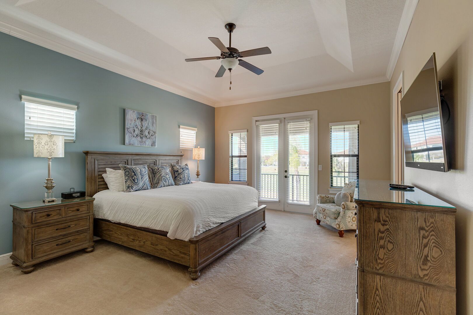 A bedroom with a bed, nightstands, a chair, a dresser, a ceiling fan, and a TV.