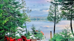 Une vue sur le lac, avec des chaises Adirondack rouges et un sentier rocheux menant à un quai.