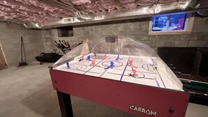 Une table de baby-foot dans un sous-sol, avec un isolant au plafond et un téléviseur fixé au mur.