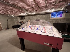 Une table de baby-foot dans un sous-sol, avec un isolant au plafond et un téléviseur fixé au mur.