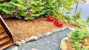 Un escalier en bois mène à une terrasse où se trouvent des fauteuils Adirondack rouges, et un chemin de gravier bordé de pierres.