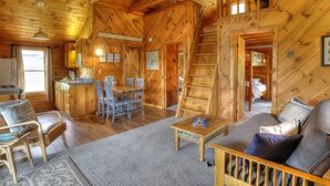A cozy cabin with a dining area, a living room with a sofa, and a staircase leading to a loft bedroom. - Hunter Cove Cabin #3: Shared Rangeley Lakefront, Dock Slip + Screened Porch (Rangeley)
