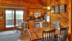 A wooden cabin interior with a dining area, kitchen, and sliding glass doors leading to a deck. - Hunter Cove Cabin #3: Shared Rangeley Lakefront, Dock Slip + Screened Porch (Rangeley)