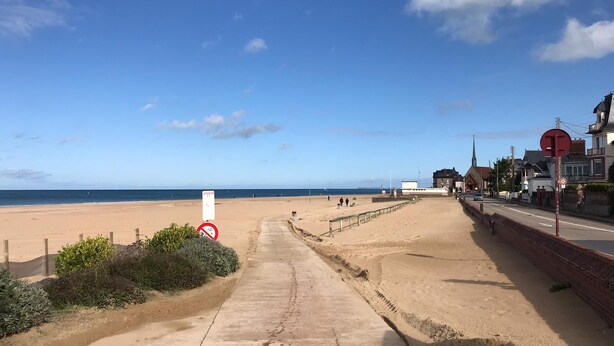 Una carretera junto a la playa con una señal de prohibido el paso, una playa de arena y edificios al fondo.