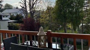 Un balcón con sillas de mimbre y una mesa, con vistas a una zona residencial con árboles y casas.