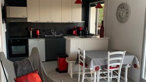 Una cocina moderna con armarios blancos, un comedor con mesa y sillas, y un mantel con estampado rojo y blanco.